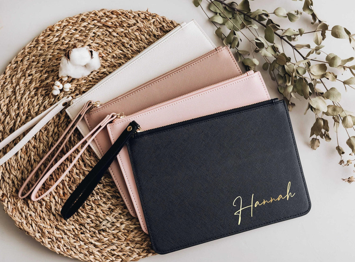 Personalized navy clutch bag with gold name on a woven tray with blush clutches