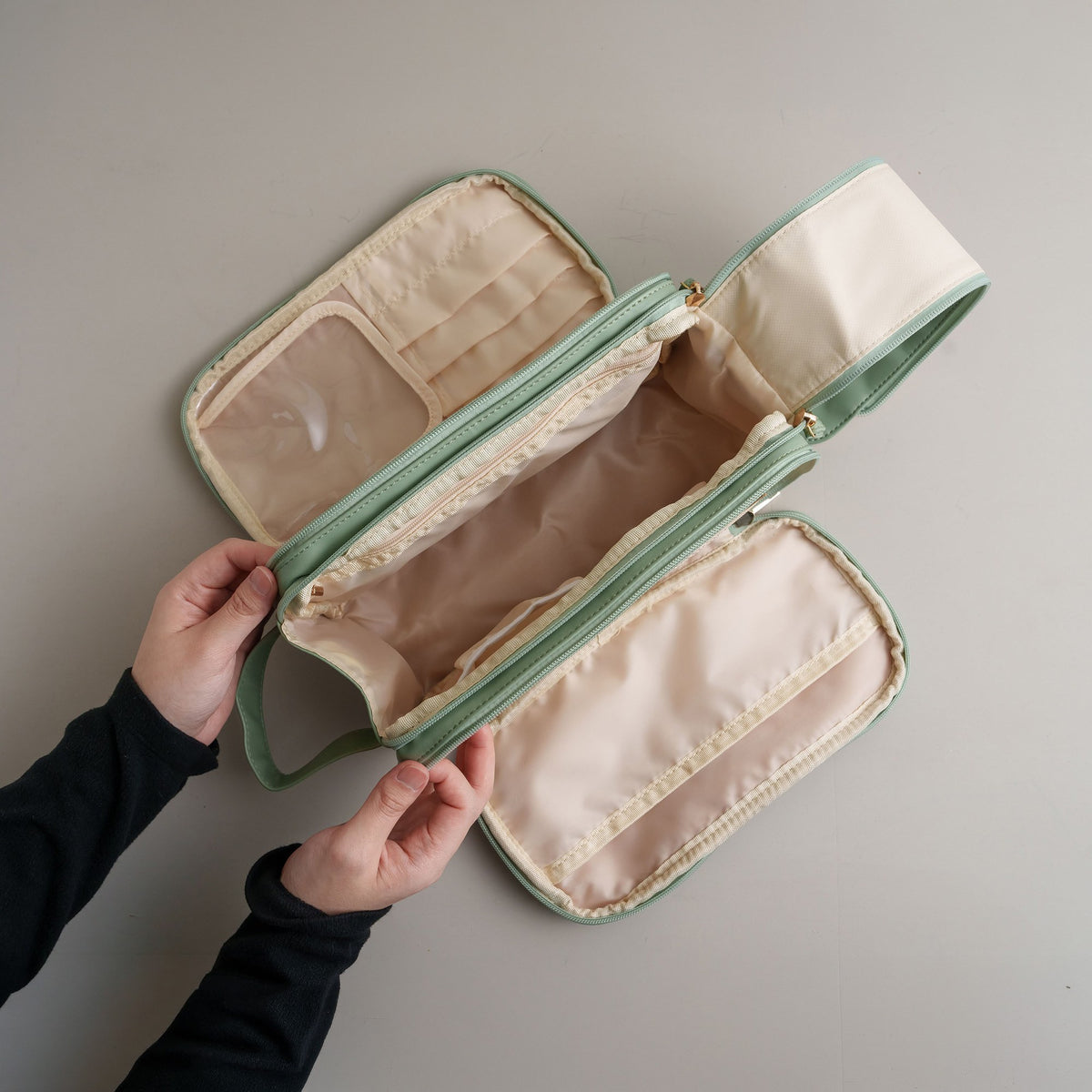 Hands opening the cosmetic bag to show the clear pocket and brush slots