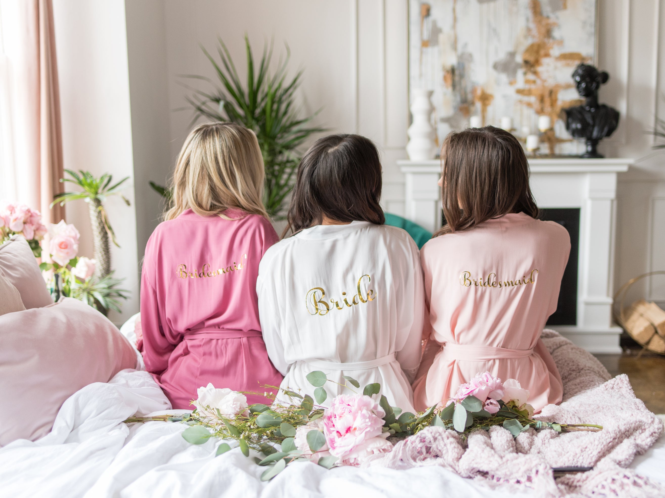 Satin Bridesmaid Robes - Three beautiful models dressed in white, blush and pink satin bridesmaid robes with monogram design in preparation for a bachelorette party, wedding or any fun occasion.