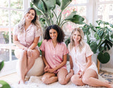 Three beautiful models dressed in white, dusty rose and blush Bridesmaid Pajamas Short Set with monogram design in preparation for a bachelorette party, wedding or any fun occasion.